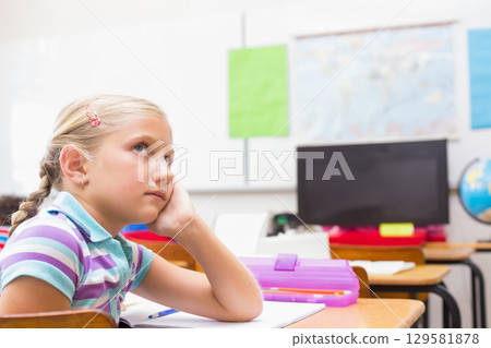 Female child student sitting at desk at school writing in notebook with pencil case, copy space 129581878