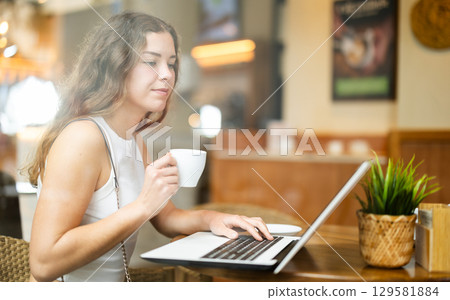 Young woman working at a laptop in a cafe Young woman working at a laptop in a cafe 129581884