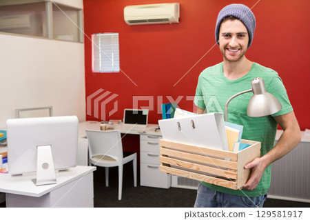 Man carrying wooden crate with office supplies in office space by red accent wall, copy space 129581917