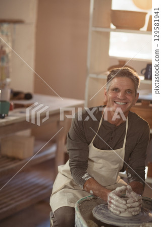 Senior male potter shaping clay on pottery wheel in workshop with clay tools on workbench Senior male potter shaping clay on pottery wheel in workshop with clay tools on workbench 129581941