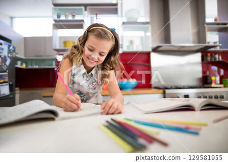 Female child in blouse writing in notebooks on kitchen counter with pink pencil and colored pencils Female child in blouse writing in notebooks on kitchen counter with pink pencil and colored pencils 129581955
