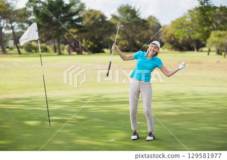 Female golfer in golf attire holding putter and celebrating on green with flagstick, copy space Female golfer in golf attire holding putter and celebrating on green with flagstick, copy space 129581977