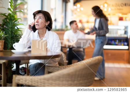 Elderly woman talking on phone in cafe 129581985