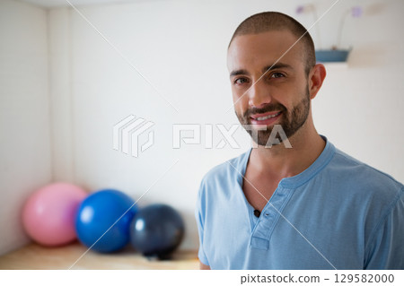 Male fitness instructor standing in yoga studio wearing blue henley near exercise balls, copy space Male fitness instructor standing in yoga studio wearing blue henley near exercise balls, copy space 129582000