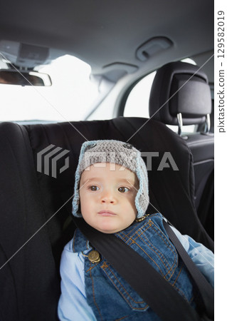 Male toddler sitting in car child safety seat wearing grey hat and overalls looking at window Male toddler sitting in car child safety seat wearing grey hat and overalls looking at window 129582019