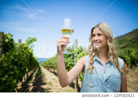 Woman wearing denim shirt holding wine glass examining white wine in vineyard rows, copy space Woman wearing denim shirt holding wine glass examining white wine in vineyard rows, copy space 129582021