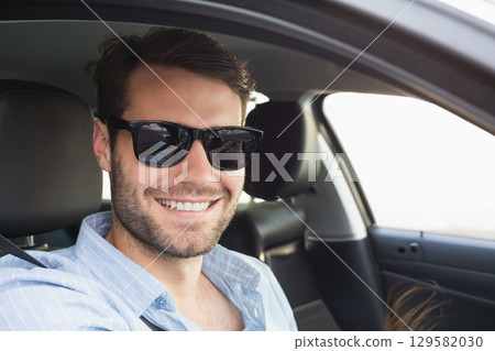Man smiling while driving in sedan with seat belt on wearing striped shirt and dark sunglasses Man smiling while driving in sedan with seat belt on wearing striped shirt and dark sunglasses 129582030