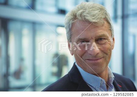 Senior male standing in office lobby wearing suit, checkered shirt by glass partitions, copy space 129582085