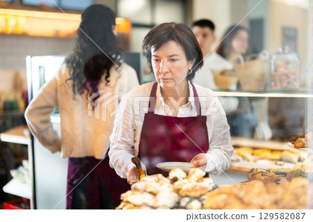 Senior woman salesperson works in cafeteria bakery shop Senior woman salesperson works in cafeteria bakery shop 129582087