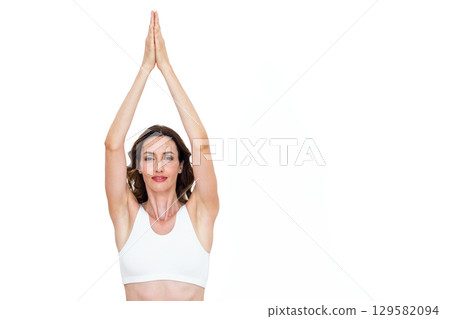 Woman raising arms above head while holding palms together and wearing sports bra in studio 129582094
