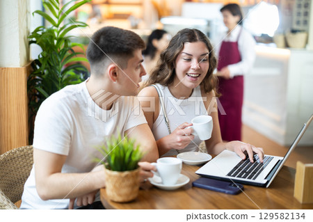 Couple man and woman with laptop drinking coffee and talking Couple man and woman with laptop drinking coffee and talking 129582134