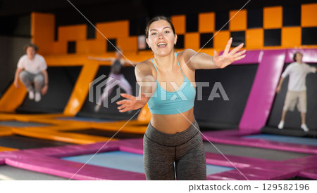Portrait of cheerful young female in sportswear posing and smiling at camera on colorful trampoline in game club 129582196