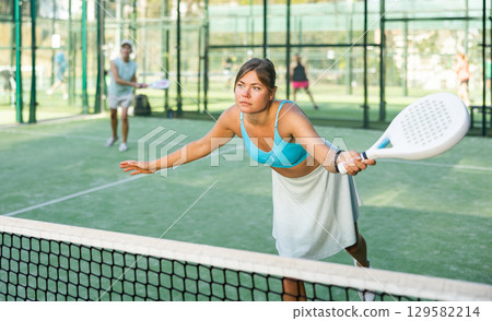 Woman playing padel tennis match during training on court 129582214
