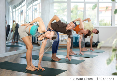 Attractive girl in sportswear using mat spend free time doing yoga for health and wellness together with group of people 129582223