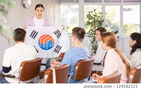 Young woman teacher holding flag of South Korea in front of group of students 129582225