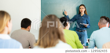 Group of students attentively listening to lecture of female teacher Group of students attentively listening to lecture of female teacher 129582435
