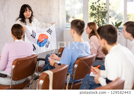 Young woman teacher holding flag of South Korea in front of group of students 129582443