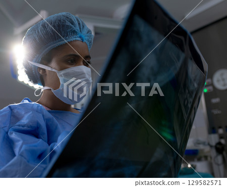 African American female surgeon examining X-ray film against surgical lamp in operating room 129582571