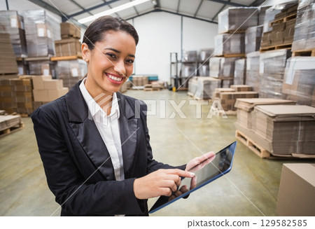 Female warehouse manager standing by pallet racks holding tablet inspecting inventory, copy space 129582585