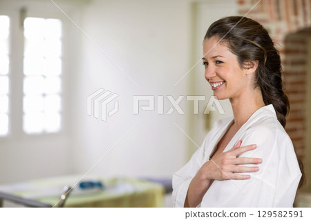 Woman wearing white robe wrapping arms across chest in spa room with massage table, copy space Woman wearing white robe wrapping arms across chest in spa room with massage table, copy space 129582591