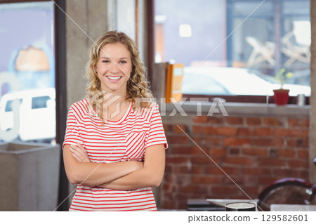 Teenage girl standing with arms crossed by brick wall in workspace by desk with file folder 129582601