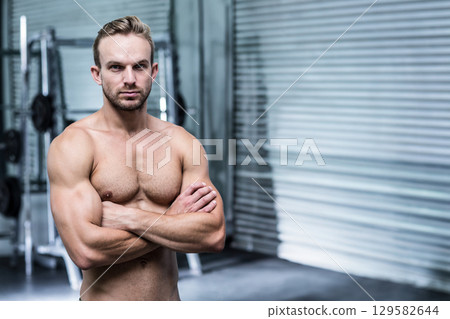 Shirtless man standing with crossed arms at gym weight rack and weights, shutter door, copy space Shirtless man standing with crossed arms at gym weight rack and weights, shutter door, copy space 129582644