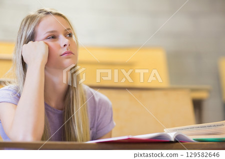 Teenage female student in purple T-shirt looking aside at open textbook on lecture desk, copy space Teenage female student in purple T-shirt looking aside at open textbook on lecture desk, copy space 129582646