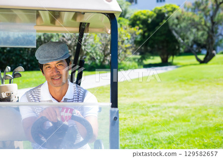 Asian man driving golf cart on golf course with golf bag wearing flat cap, copy space Asian man driving golf cart on golf course with golf bag wearing flat cap, copy space 129582657