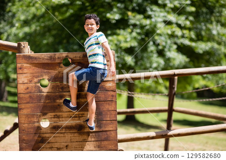 Female child climbing wooden panel with round holes at park playground near chain links, copy space 129582680