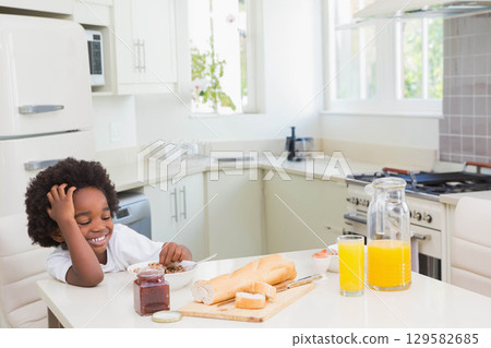 African American child eating from bowl of cereal at kitchen table by juice jug, copy space 129582685