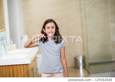 Female child brushing teeth in bathroom at countertop sink with toothbrush and wooden cabinet 129582686