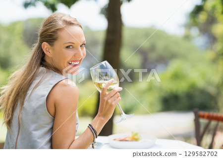 Woman smiling and holding stemmed glass at outdoor cafe table with plate of food and bracelets Woman smiling and holding stemmed glass at outdoor cafe table with plate of food and bracelets 129582702