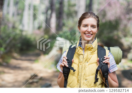 Woman standing on forest trail wearing yellow vest and holding hiking backpack with sleeping mat Woman standing on forest trail wearing yellow vest and holding hiking backpack with sleeping mat 129582714