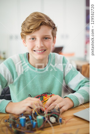 Teenage boy assembling electronic circuit at workshop desk using breadboard with wires and laptop 129582720