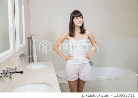 Woman standing with hands on hips in bathroom examining dual sink marble vanity and bathtub Woman standing with hands on hips in bathroom examining dual sink marble vanity and bathtub 129582731