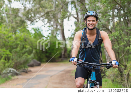 Man riding mountain bike on dirt trail in forest wearing cycling helmet and hydration backpack 129582738