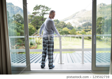 Man standing holding white balcony railing and looking over green lawn toward distant hills Man standing holding white balcony railing and looking over green lawn toward distant hills 129582739