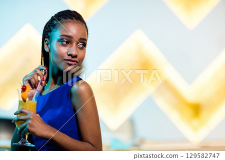 African American teenage girl holding glass of orange cocktail in blue dress at bar, copy space African American teenage girl holding glass of orange cocktail in blue dress at bar, copy space 129582747