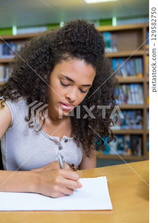 African American woman writing on blank paper with pen at library table under lights African American woman writing on blank paper with pen at library table under lights 129582750