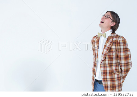 Man standing clasping hands behind back in studio wearing blazer and bow tie, copy space 129582752