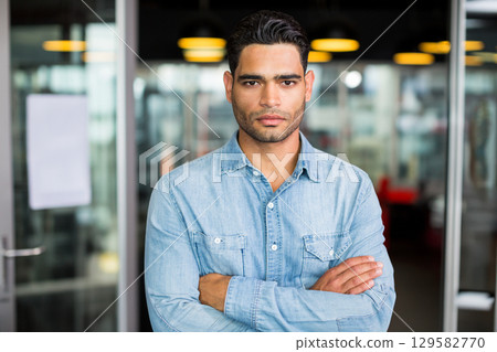 Man standing facing forward in office hallway wearing shirt under pendant lamps and glass door 129582770