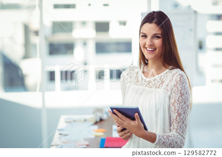 Woman in lace blouse smiling by window holding tablet at office desk with papers, copy space Woman in lace blouse smiling by window holding tablet at office desk with papers, copy space 129582772