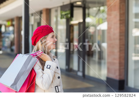 Woman standing on shopping street holding pink and gray paper bags near storefront, copy space 129582824