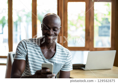 African American man sitting at wooden table in coffee shop using laptop and smartphone African American man sitting at wooden table in coffee shop using laptop and smartphone 129582875