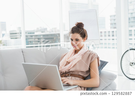 Female professional sitting on sofa in office lounge working on silver laptop with bicycle frame 129582887