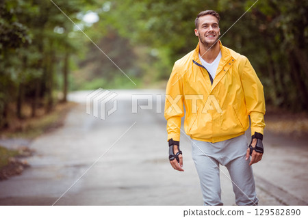 Male skater gliding on forest path wearing windbreaker wrist guards and inline skates, copy space 129582890