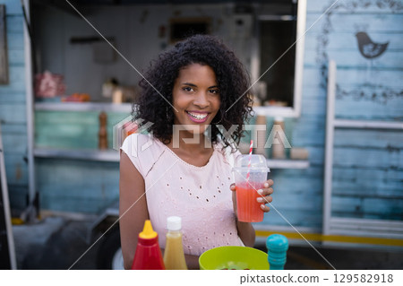 African American woman sitting at teal food truck holding cup with striped straw and condiments 129582918
