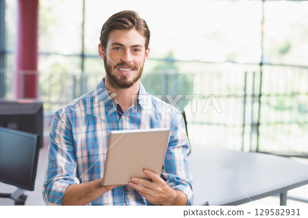 Bearded man holding tablet in open-plan office with computer monitors and metal railing 129582931