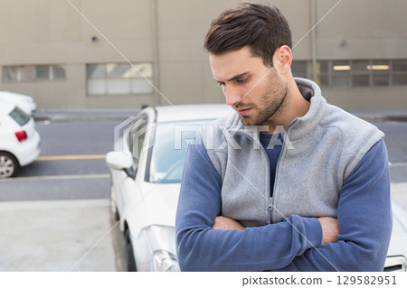 Man standing with crossed arms in parking area near beige building and white sedan, copy space 129582951