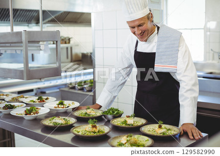 Male chef inspecting plated seafood and grains on kitchen counter under heat lamp, copy space 129582990